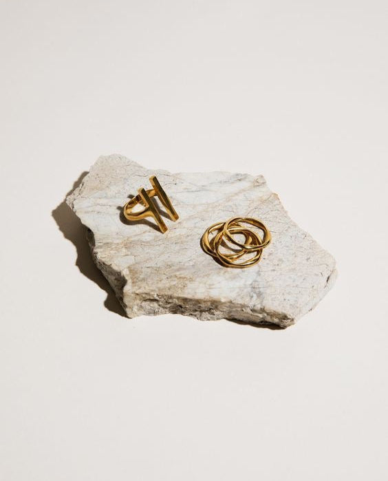 Anillos dorados con diseño escultórico sobre piedra de mármol — composición minimalista y atemporal